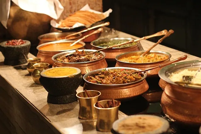 A traditional Bengali wedding buffet spread featuring various traditional dishes served in elegant, hammered copper handis (pots) with brass serving spoons. The counter includes a variety of curries, a mixed vegetable dish, rice, and traditional accompaniments in stone and brass bowls under warm lighting organised by Food Chakra – Trusted Catering Services in Kolkata