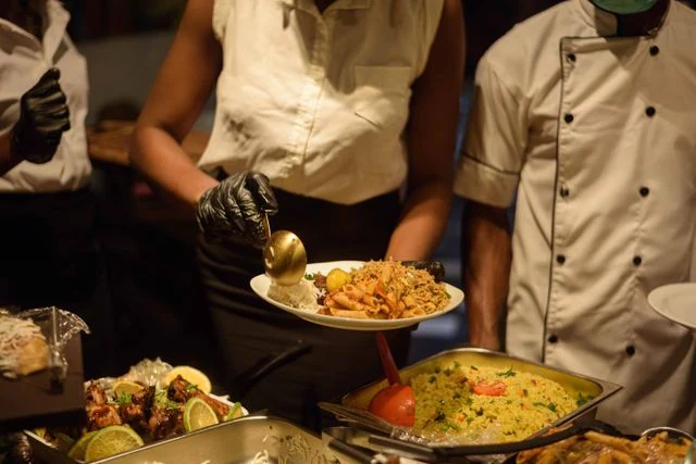 Professional catering staff wearing black safety gloves and white uniforms serving premium buffet dishes, including fried rice and pasta, at a wedding event. This hygienic live buffet service in Kolkata is provided by Food Chakra.