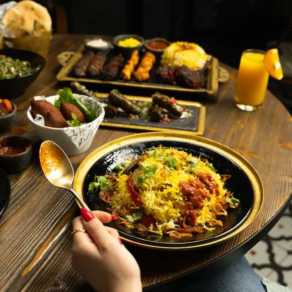 A gourmet multi-cuisine dining table featuring a premium plate of saffron-infused aromatic rice garnished with fresh coriander and fried onions. The spread includes grilled kebabs, platters of appetizers, and fresh orange juice, highlighting the premium wedding and reception catering menus by Food Chakra in Kolkata. | Image for Food Chakra – Trusted Catering Services in Kolkata